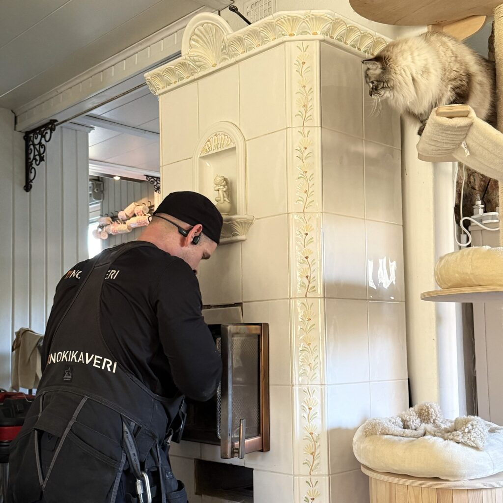 Kissa katsomassa nuohoojan työskentelyä takan ääressä